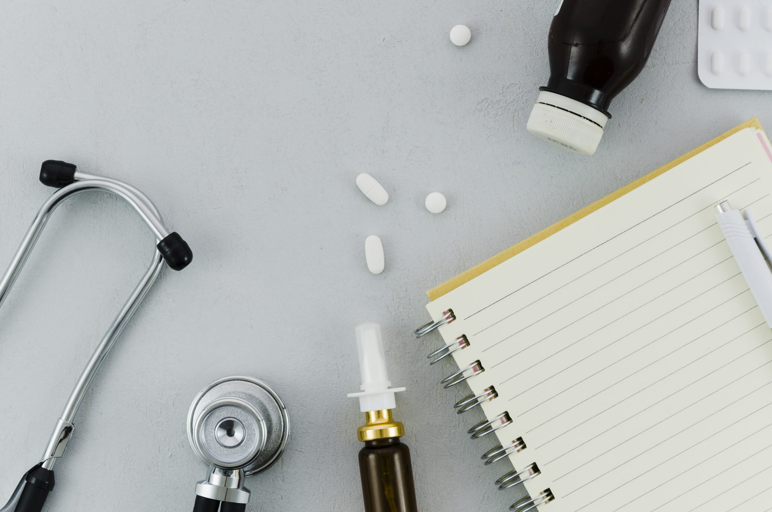 stethoscope-pills-bottle-nasal-spray-diary-pen-grey-background