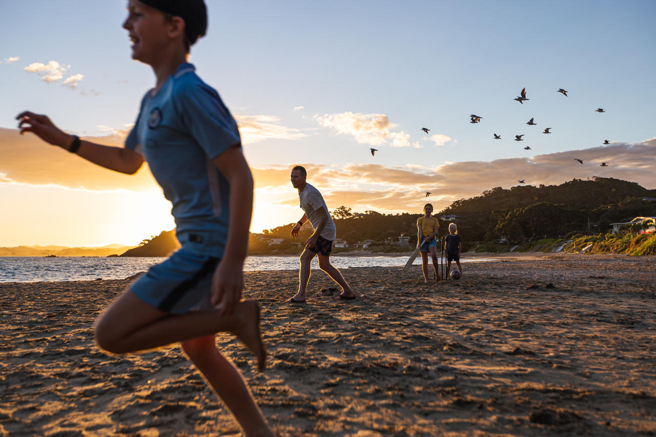 A family plays cricket on the beach at sunset 